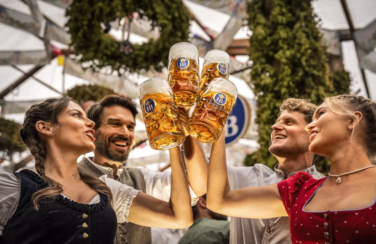 Freundesgruppe stößt im Hofbräuzelt auf dem Oktoberfest mit Maßkrügen mit Bier an