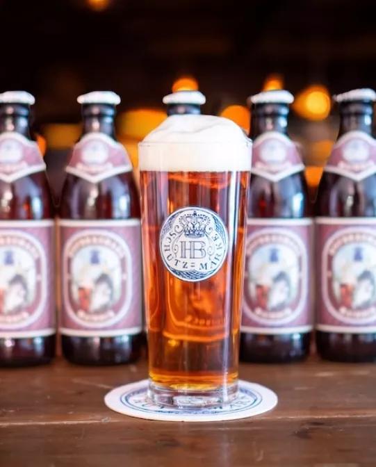 Hofbräuhaus Maibock im Glas mit Schaumkrone und Bierflaschen