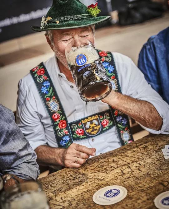regular in bavarian traditional outfit drinking dark beer