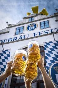 Masskrüge vor Hofbräu Festzelt mit Himmel und Krone im Hintergrund