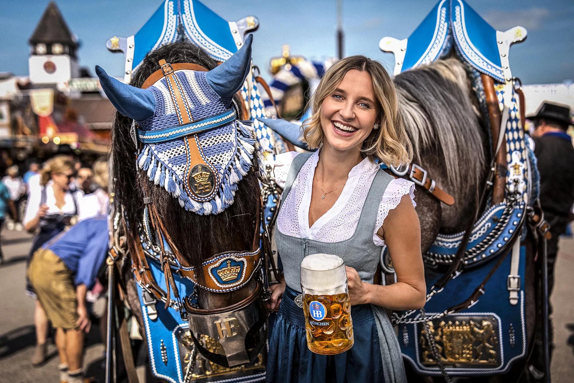 Frau in Tracht mit Masskrug mit Bier auf Oktoberfest mit Pferdegespann