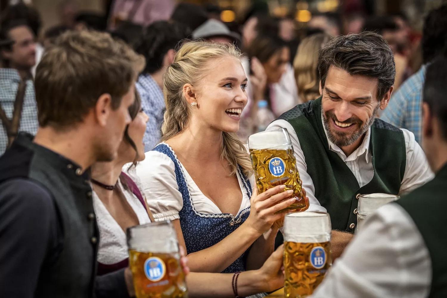 Frau mit Freundesgruppe an Tisch im Hofbräu Festzelt mit Masskrug in der Hand
